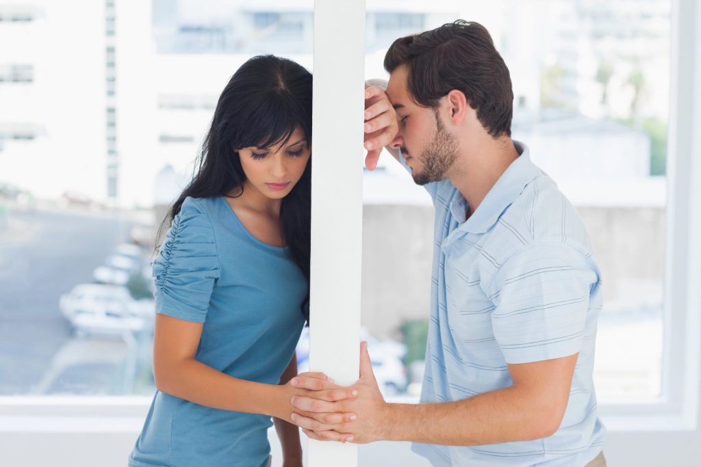 A man and woman leaning against opposite sides of a wall, looking contemplative and concerned.
