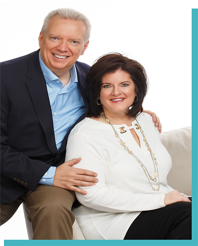 A smiling couple sits together, dressed in business attire.