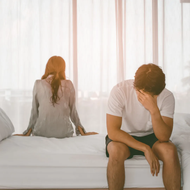 A couple sits on a bed facing away from each other; the scene suggests a possible marital crisis.